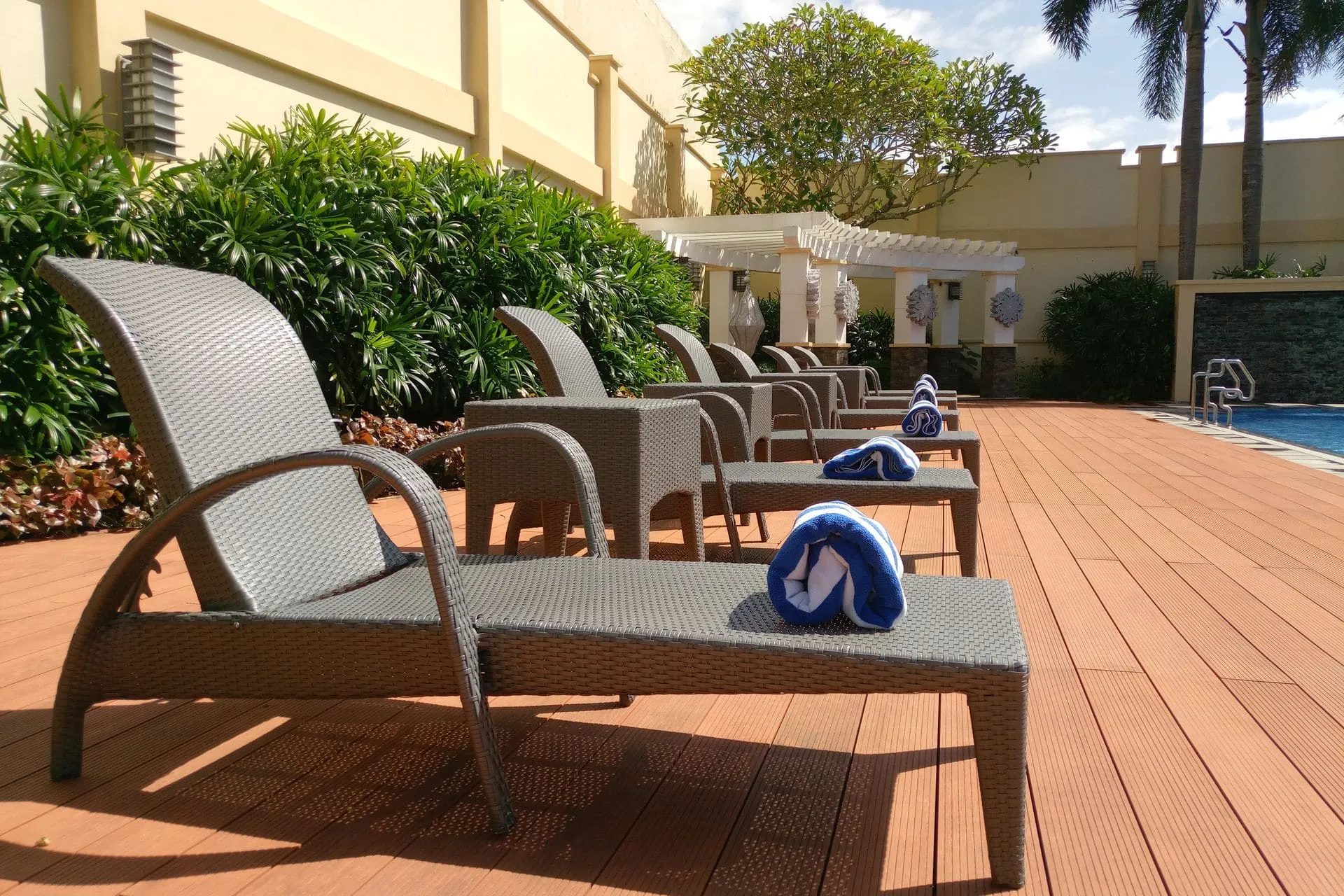 Timber pool decking with sun loungers beside a swimming pool in warm sunshine