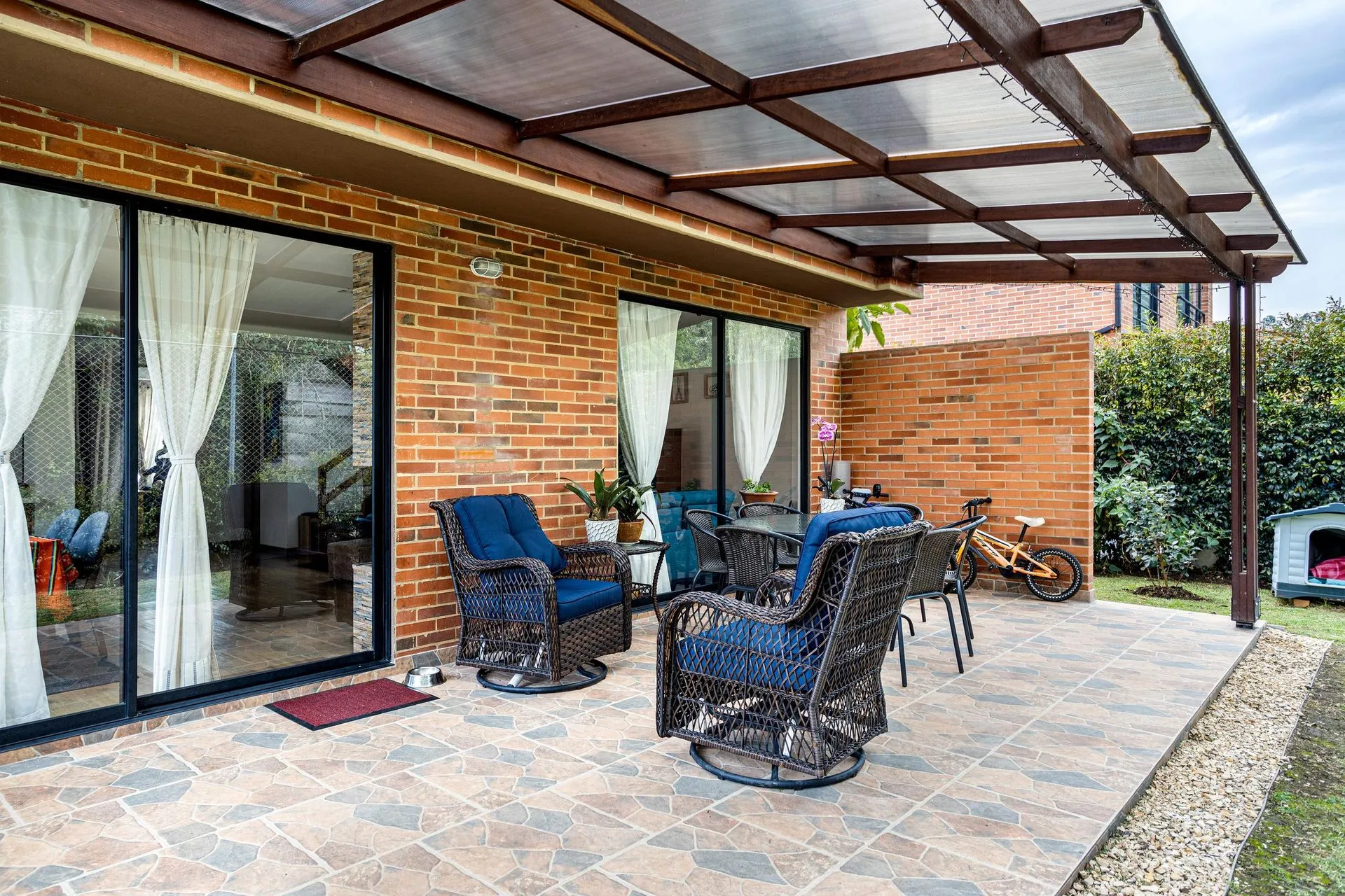 Clear-roofed patio cover over paved outdoor seating beside a brick home