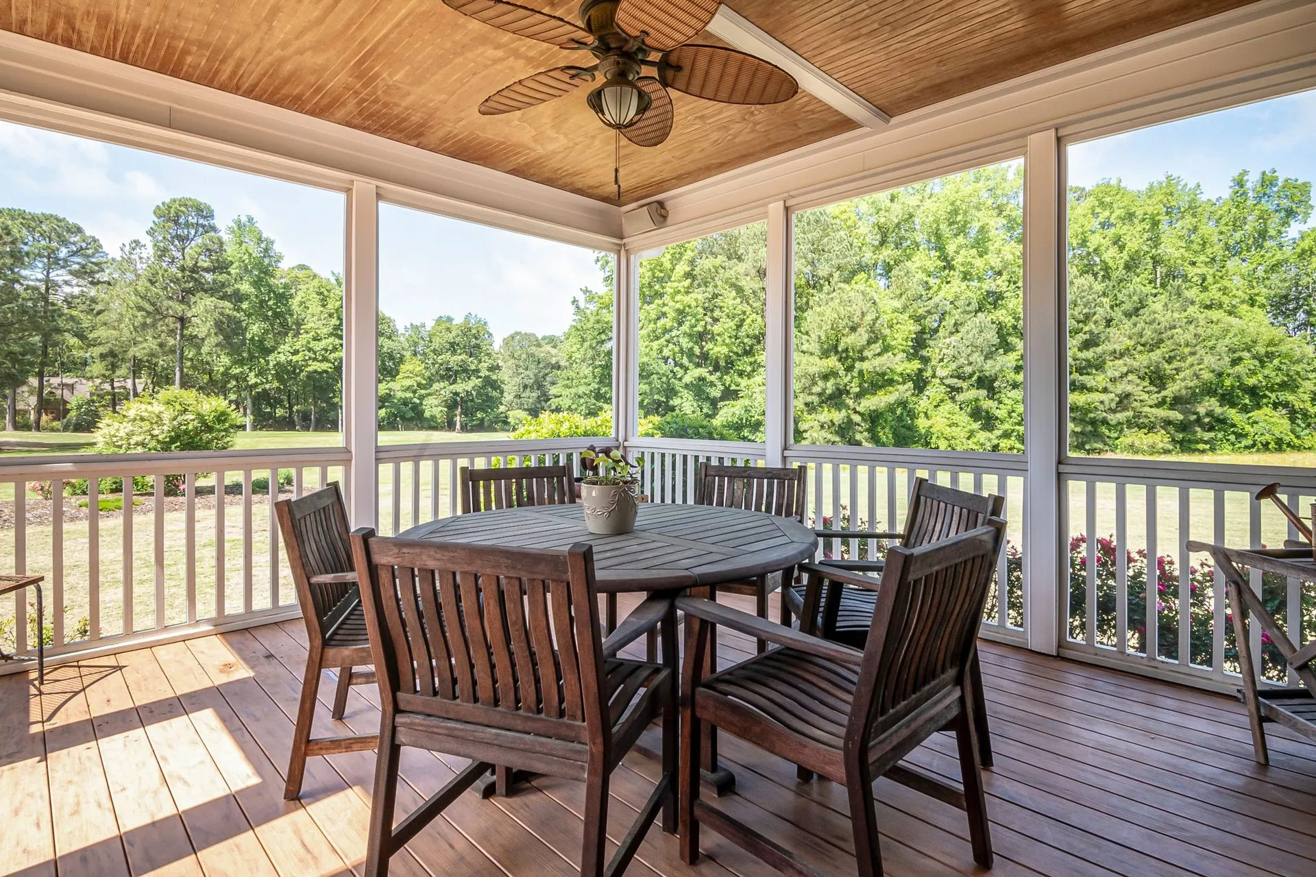 Roofed timber deck with a dining table and ceiling fan, looking out over trees